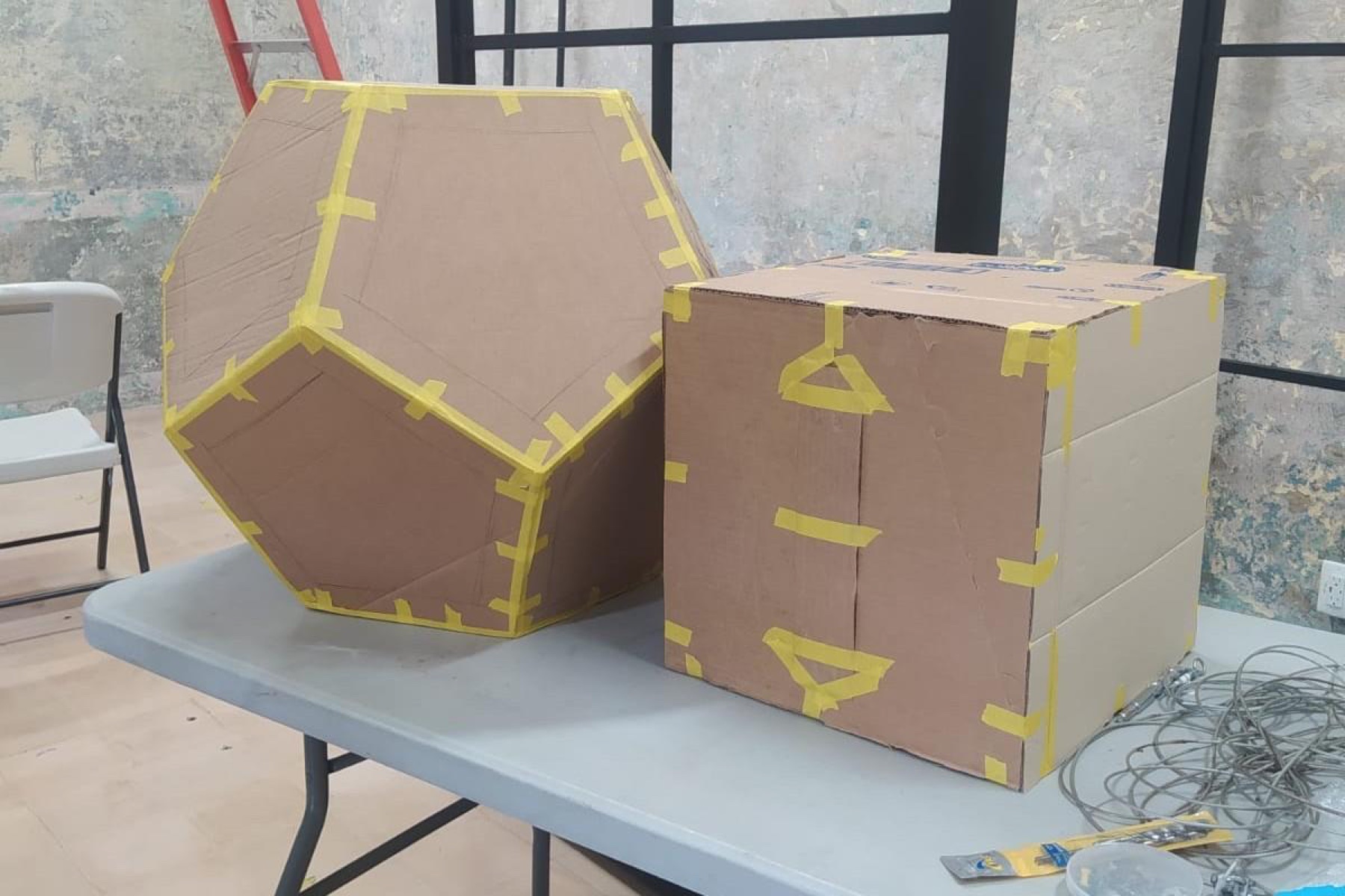 Dos prototipos de cartón sobre una mesa: un dodecaedro y un cubo