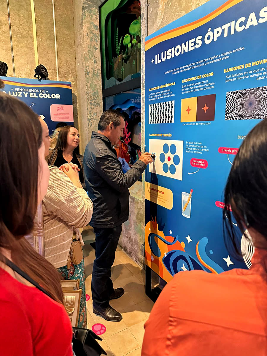Visitantes leen y tocan el panel de ilusiones ópticas en la sala