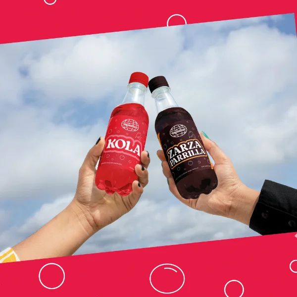 Dos manos chocan dos botellas de refresco frente a un cielo con nubes, sobre un marco rojo